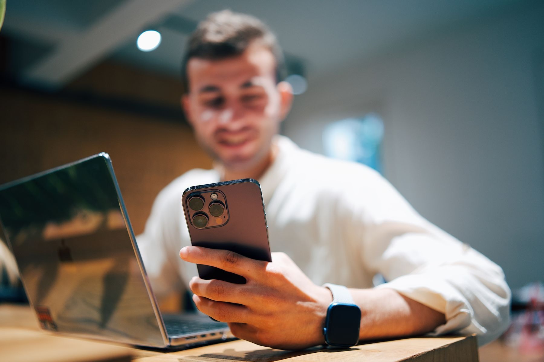 Collaborateur utilisant un smartphone et un ordinateur portable dans un bureau.
